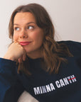 Person wearing a navy blue sweatshirt with 'MINNA CANTH' text, sitting on a white surface.